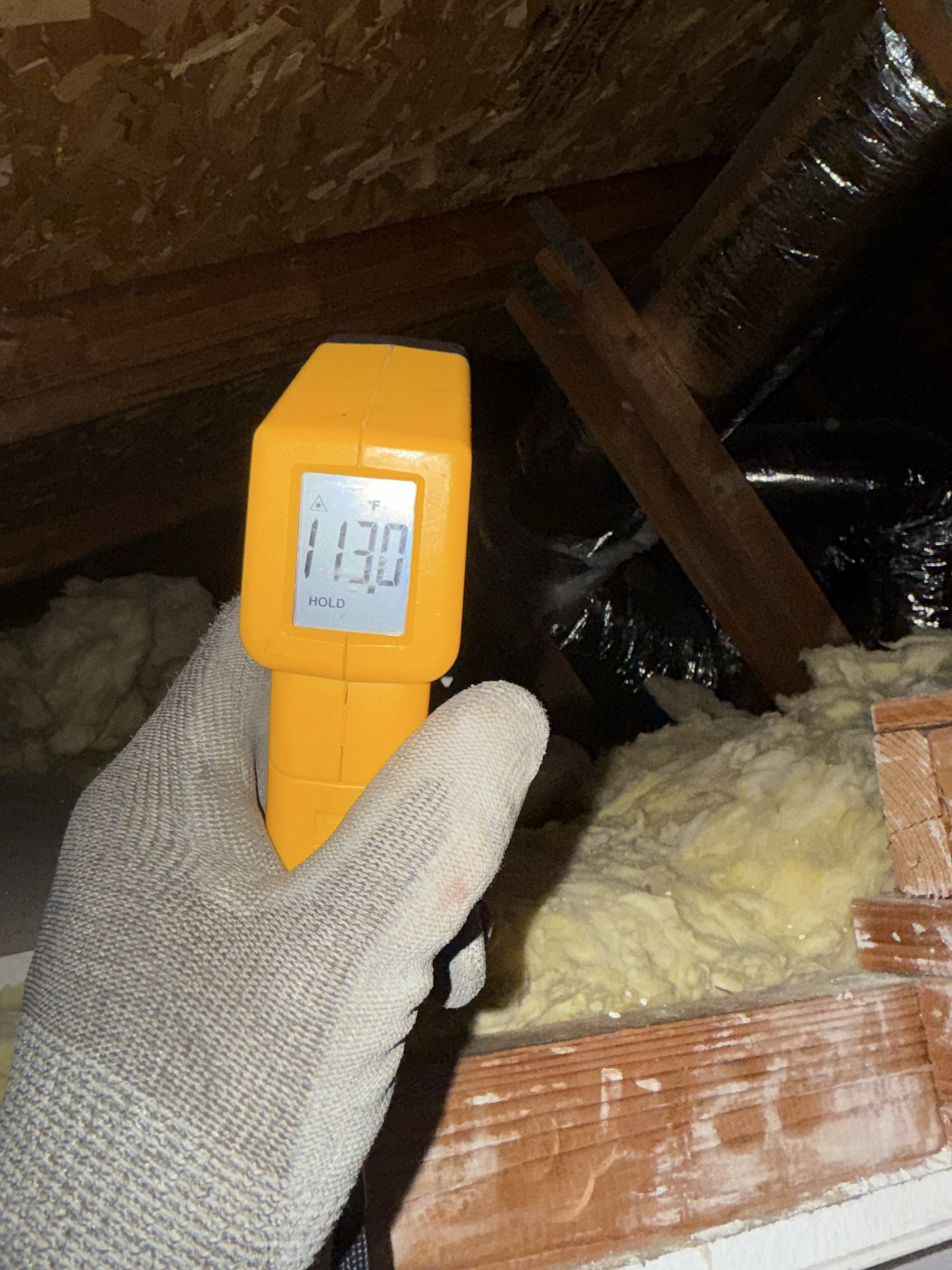 Infrared thermometer reading 113°F during attic HVAC diagnostic